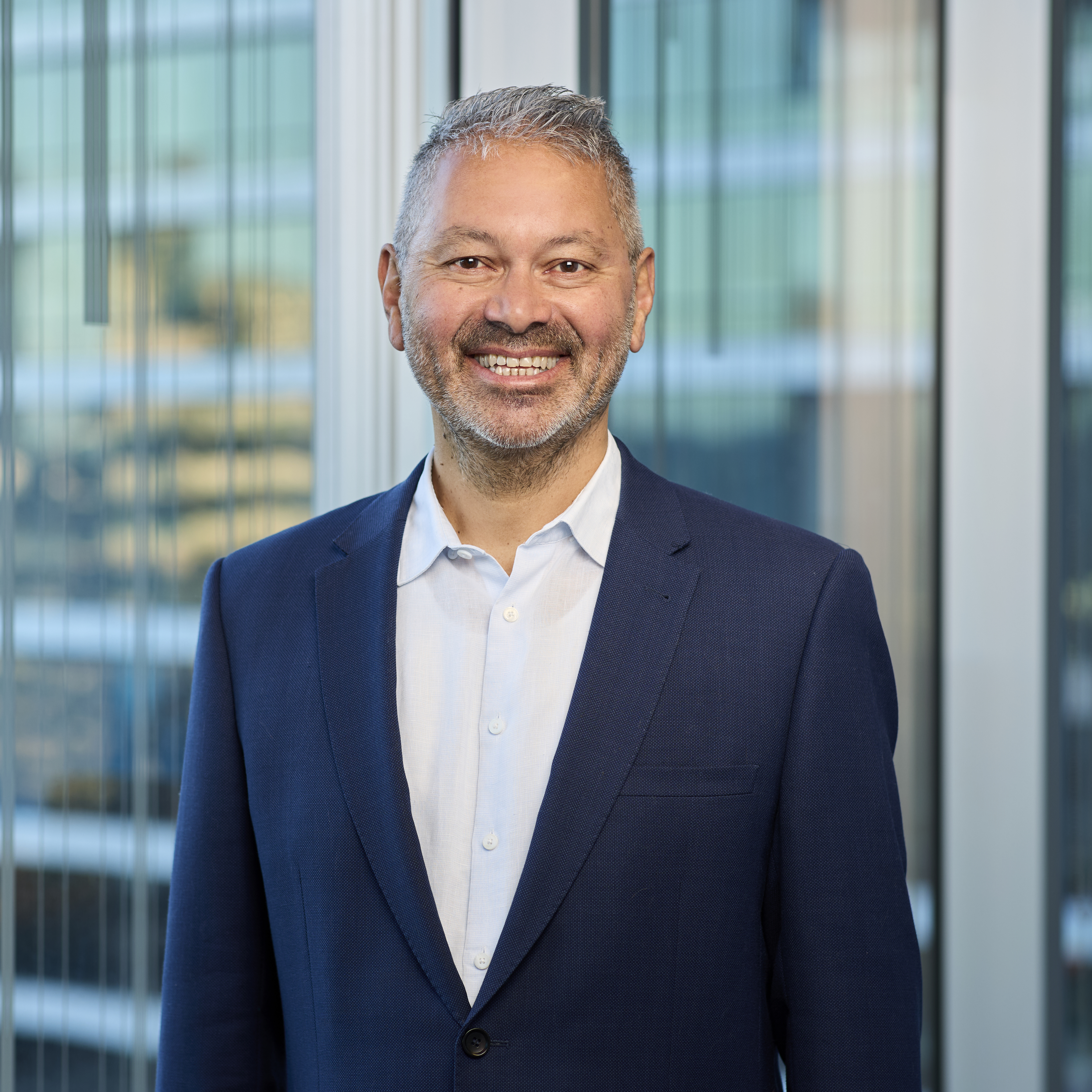 Maha Krishnapillai smiling in a navy suit and white collared shirt.