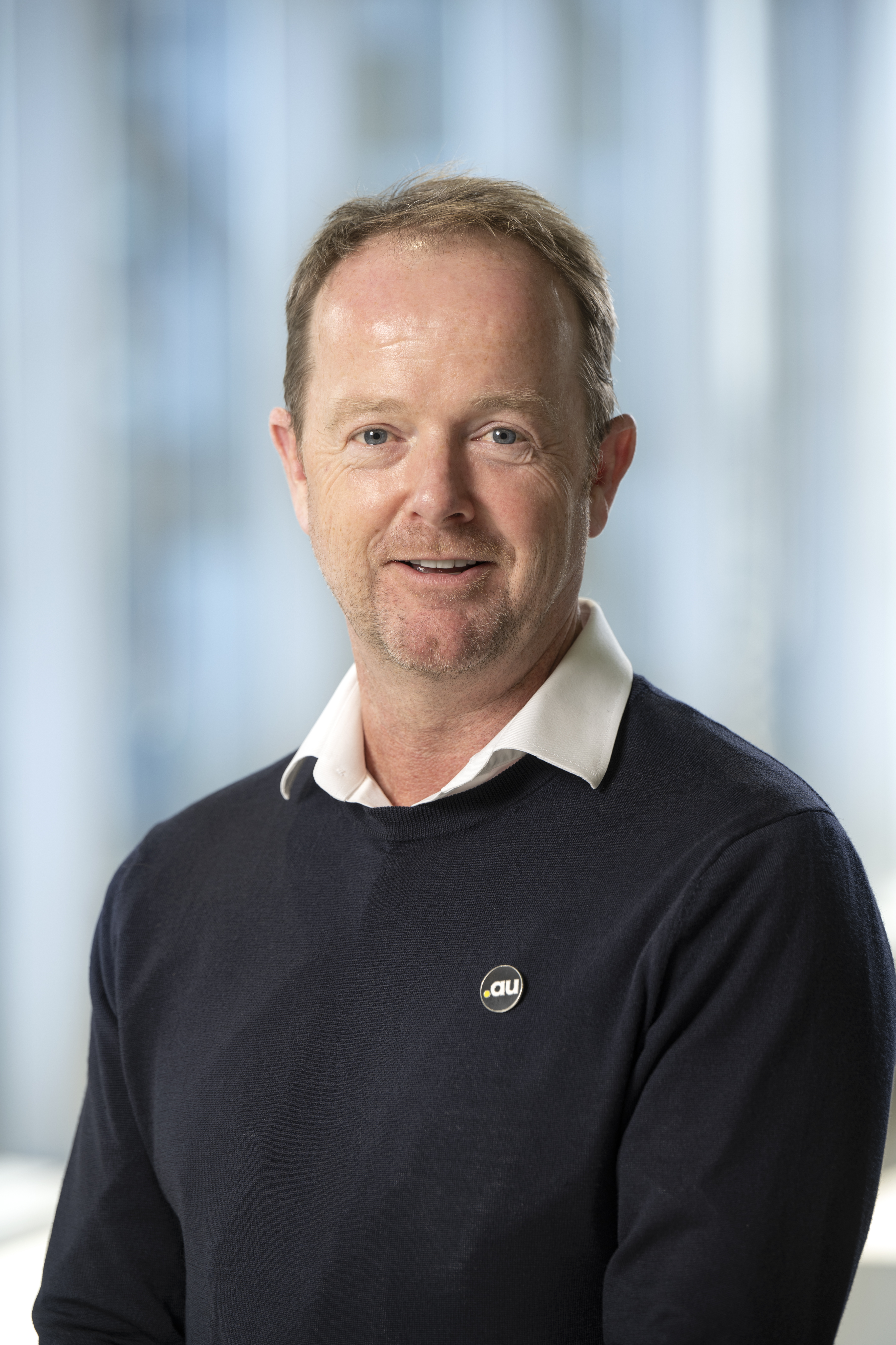 Matt Healy smiling wearing a charcoal skivvy over a white collared shirt.