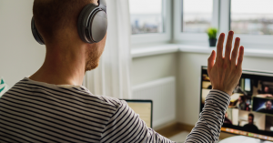 Man waves to computer screen. Screen shows online webinar.